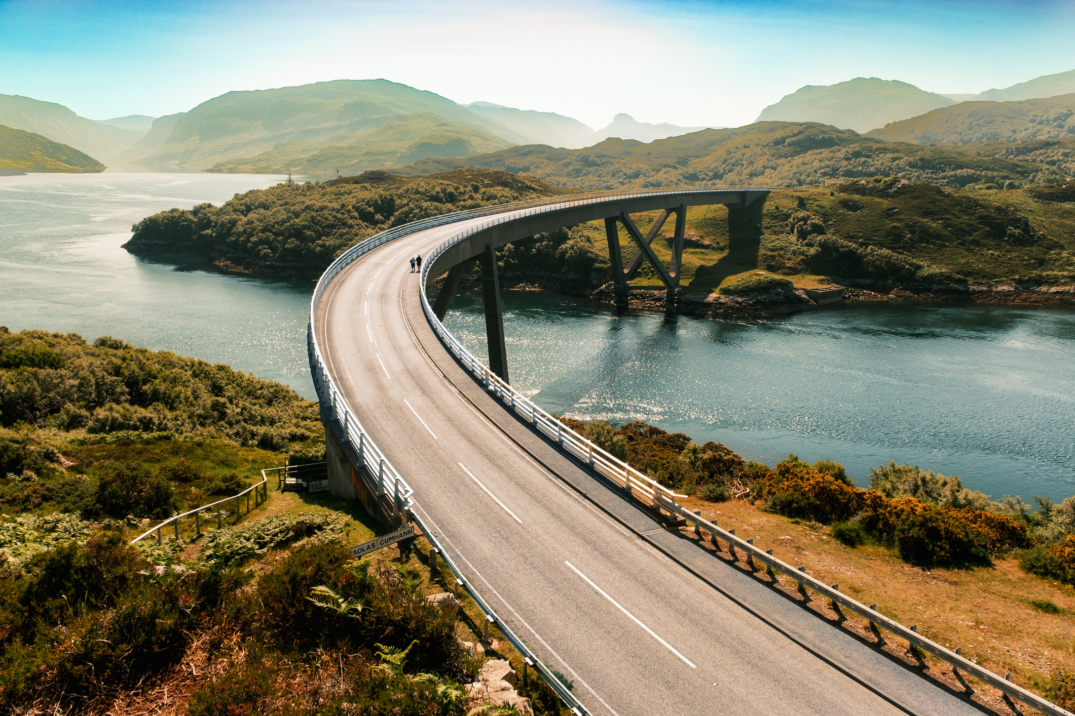 Curved coastal bridge crossing a sea loch with hills in the background.