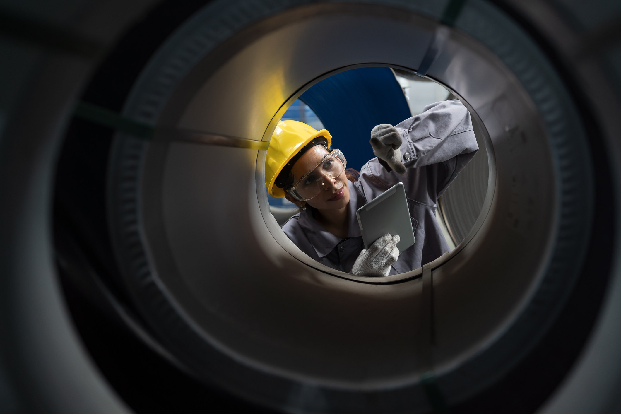 Worker inspecting industrial piping while using a tablet.