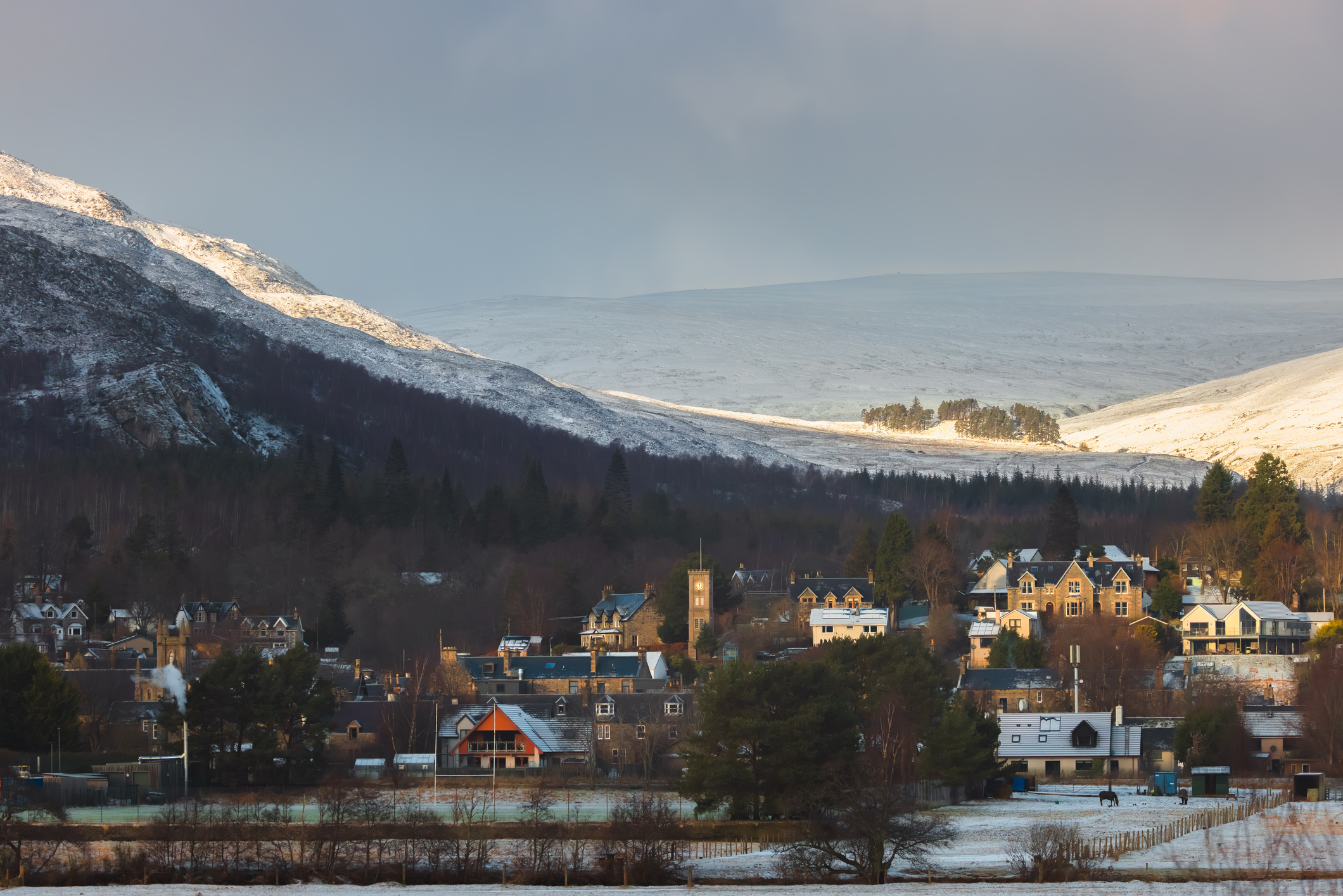 Snow-covered Scottish village beneath hills.