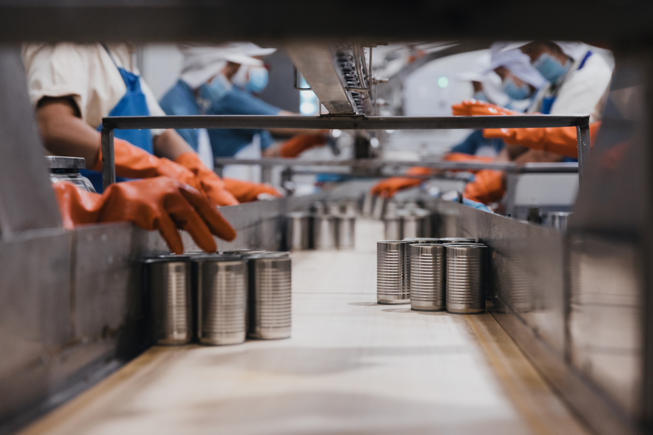 Workers handling food cans on a production line in a food processing facility.